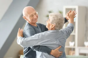 Two elderly people dancing together in a cozy living room, smiling as they hold each other.
